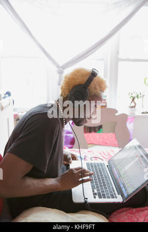 Junger Mann mit der Eingabe auf seinem Laptop mit Kopfhörern Stockfoto