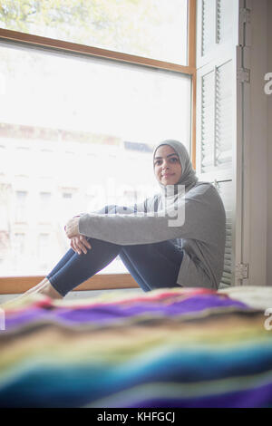 Muslimische Frau trägt ein Kopftuch auf dem Fensterbrett sitzen Stockfoto