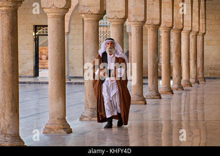 Ein Einheimischer in ethnischer Kleidung, der durch die Säulen im Innenhof der Mevlidi-Halil-Moschee in Sanliurfa, Türkei, geht. Stockfoto