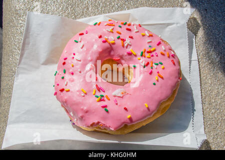 Große rosa iced Donut auf eine Papiertüte Stockfoto