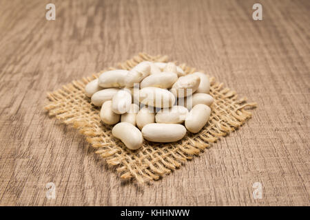 Phaseolus vulgaris ist wissenschaftlicher Name der Marine Bohne Hülsenfrucht. Auch bekannt als weiße, pearl Bean und feijao Branco. Körner am eckigen Ausschnitt aus Jute. woode Stockfoto