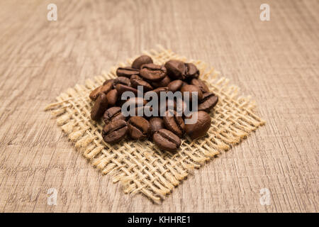 Auswahl von gerösteten Kaffeebohnen Saatgut. Körner am eckigen Ausschnitt aus Jute. Holztisch. Selektive konzentrieren. Stockfoto