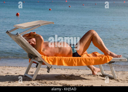 Ältere Menschen, die auf einer Sonnenliege am Strand Stockfoto