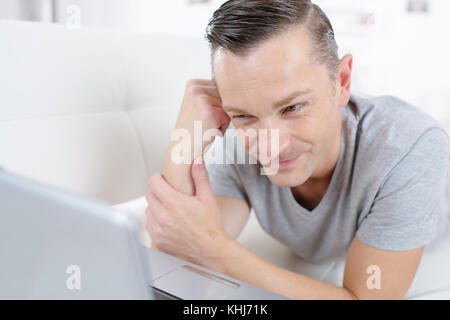 Ein Mann auf dem Sofa schaut tv am Laptop Stockfoto