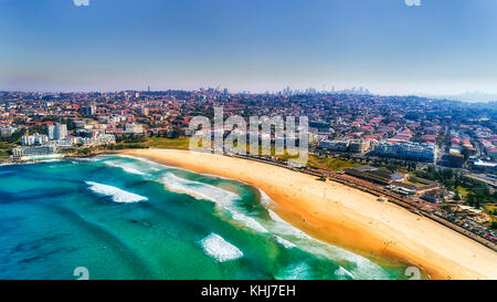 Welle bricht und surfen Sie auf klare Sand des berühmten australischen Sydney Bondi Beach in Luftaufnahme mit Innenstadt im Hintergrund. Stockfoto