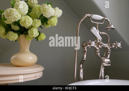 Einen schönen Blumenstrauß Schneeball Blumen in einer Vase, neben altmodischen Badewanne Armaturen im Badezimmer. Stockfoto