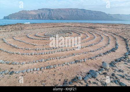 Runde Steine am Boden bildet eine Spirale, in der Nähe des Strandes, mit Lanzarote im Hintergrund, Caleta del Sebo, La Graciosa, Kanarischen Insel Stockfoto