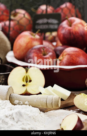 Alte hölzerne Rolling Pin bestäubt mit weißem Mehl über eine rustikale Tisch. Apfelkuchen Zutaten von Äpfeln und Butter im Hintergrund. Extrem flache Dept Stockfoto