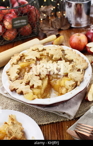 Frisch gebackenen Apfelkuchen mit oberen Kruste in autumn leaves Form und Stück fehlt. die Äpfel im Hintergrund. Stockfoto