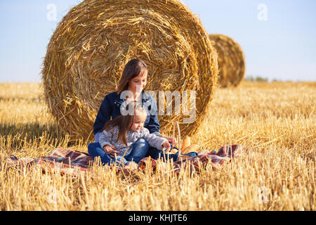 Glückliche Mutter und 2 Jahre alten Mädchen neben Heuballen in geernteten Feld Stockfoto