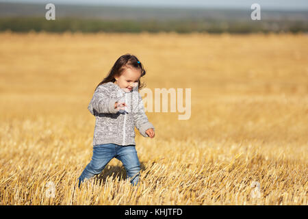 Happy 2 jähriges Mädchen zu Fuß in einer Sommer geernteten Feld Stockfoto