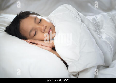 Junge schlafend auf dem Bett mit weißen Laken und Kissen. Die asiatischen Kind einschlafen Träumen. Schlaf Konzept Stockfoto