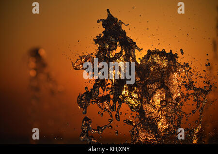 Wasser spritzen auf Sonnenuntergang farben Hintergrund isoliert. Stockfoto