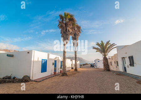 Blick auf einen typischen Straße mit einigen Palmen im Vordergrund und der Strand im Hintergrund, La Graciosa, Kanarische Inseln, Spanien Stockfoto