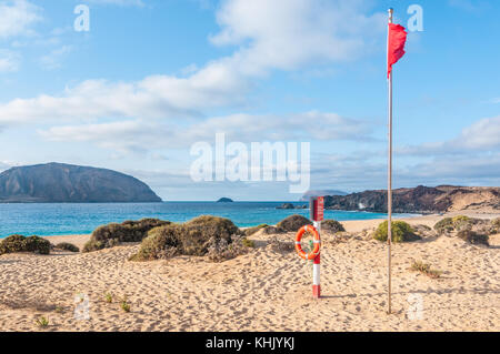 Blick auf Playa de las Conchas mit Montaña Clara Insel im Hintergrund auf der linken Seite und Roque del Infierno auf der rechten Seite mit der roten Flagge und lebensretter ich Stockfoto