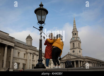 Zwei ausländische Frauen Touristen machen eine selfie von sich selbst im Stehen an der Wand gegenüber der Kirche von St. Martins und der National Portrait Gallery, die am 15. November 2017, auf dem Trafalgar Square, Westminster, London, England. Stockfoto