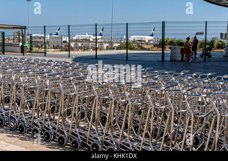 Lange Reihe mit Gepäckwagen am Flughafen Faro in Portugal (Algarve) mit Flugzeugen von Ryanair im Hintergrund. Stockfoto