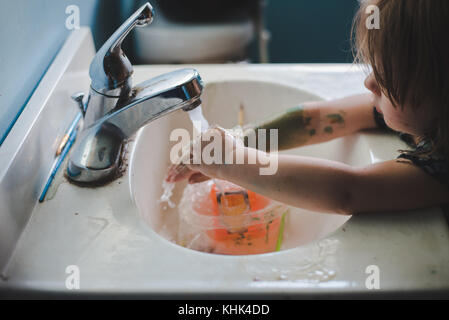 Ein Kleinkind Mädchen waschen Farbe weg die Hände in einem Waschbecken im Bad. Stockfoto