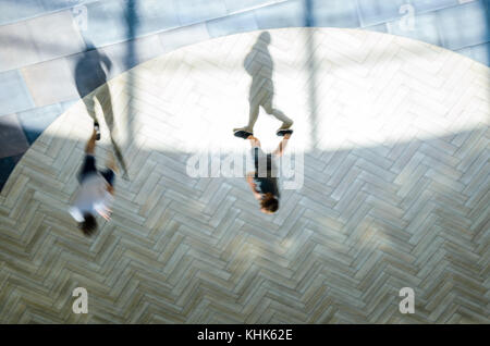 Silhouetten der beiden wandern Menschen in das Atrium eines großen öffentlichen Gebäude, die Aussicht von oben. lange Schatten. Blur in Bewegung, Langzeitbelichtung. Abstrakte bac Stockfoto