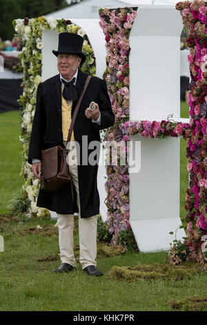 Mann zu sprechen, ist im viktorianischen Outfit & stehend gekleidet mit riesigen Blumen RHS schreiben - RHS Chatsworth Flower Show Showground, Derbyshire, England, UK. Stockfoto