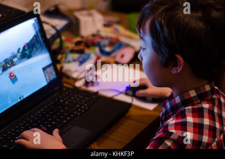 Ein kleiner Junge spielt ein Spiel auf einem Laptop in der Nacht. Stockfoto