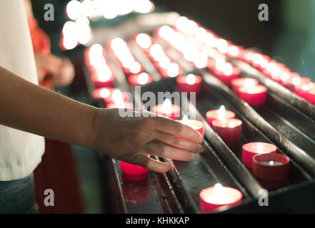 Die Frau stellt eine Kerze auf den Altar in der Kirche. Stockfoto