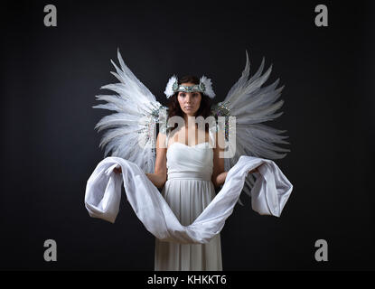 Junge schöne Frau in weißem Kleid mit Angel Wings und die Verkleidung in den Händen. Schwarzen Hintergrund. Stockfoto