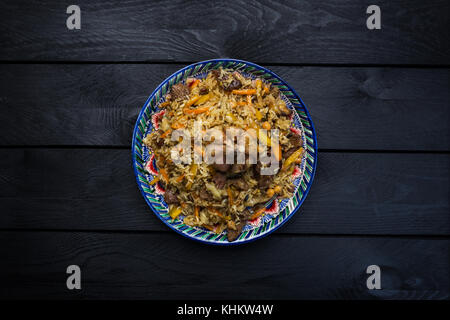 Pilav auf Platte mit orientalischen Ornament auf einer hölzernen Hintergrund. zentral-asiatische Küche - Plov. Ansicht von oben. Stockfoto