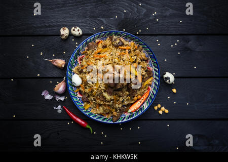 Pilav und Zutaten auf Platte mit orientalischen Ornament auf einem dunklen Hintergrund. zentral-asiatische Küche - Plov. Ansicht von oben. Stockfoto