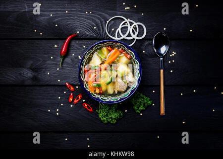 Die shurpa Suppe in den Teller mit orientalischen Ornament auf einer hölzernen Hintergrund. zentral-asiatische Küche. Ansicht von oben. Stockfoto