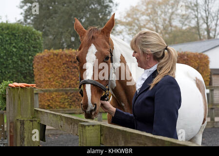 Attraktive blonde Frau mit ihrem Skewbaldpferd und ein paar Karotten. November 2017 Stockfoto