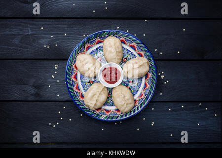 Traditionelle gedämpfte Teigtaschen manti auf Platte mit orientalischen Ornament mit Tomatensoße. top anzeigen. dunklen Hintergrund. Stockfoto