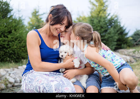 Die jungen osteuropäischen Mutter und ihren zwei kleinen Kindern sitzt auf einer Holzbank in der Natur im Sommer Tag, Kuscheln und küssen Stockfoto