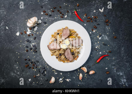 Pilav auf Platte mit orientalischen Ornament auf einem dunklen Hintergrund. zentral-asiatische Küche - Plov. Ansicht von oben. Stockfoto
