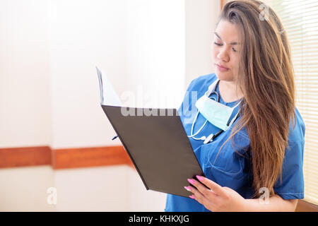 Nahaufnahme der jungen Ärztin lesen einen medizinischen Bericht in einem Krankenhaus Flur, trägt blaue Uniform mit ernsten Gesicht Stockfoto