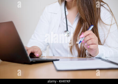 Nahaufnahme der jungen Ärztin hinter dem Schreibtisch Ausfüllen eines Formulars sitzen Stockfoto