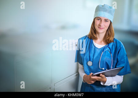 Lächelnde junge weibliche Arzt in einer blauen Uniform steht drinnen in einer Klinik, Neigung zu Metall Aktenschrank, Ordner und Suchen Stockfoto