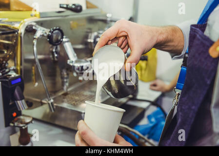 Barista mit Kaffeemaschine bereitet frischen Kaffee und Milch zu Espresso Kaffee latte Kunst in White Paper Cup im Coffee Shop. Selektive Stockfoto