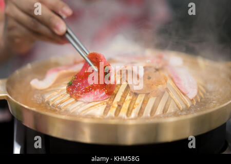 Hand mit Stäbchen mit gegrillten koreanischen Schweinefleisch vom Grill yakiniku im japanischen Stil. Stockfoto