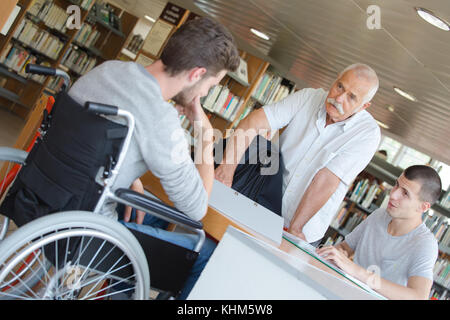 Student im Rollstuhl im Gespräch mit Lehrer in der Bibliothek Stockfoto