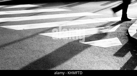 Blurry Zebrastreifen mit Silhouette und Schatten von Person zu Fuß in das kalte und sonnige Herbstwetter am frühen Morgen in Schwarz und Weiß Stockfoto