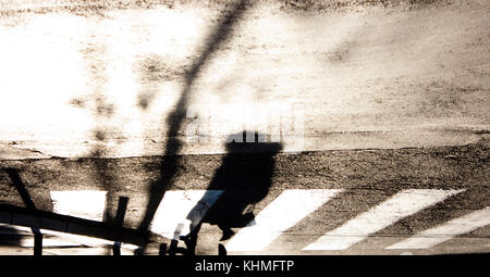 Blurry Zebrastreifen mit Silhouette und Schatten einer Frau zu Fuß in den kalten, sonnigen Herbst in Schwarz und Weiß, mit der Oberseite nach unten Stockfoto