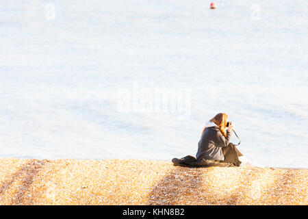 Brighton, UK. Eine junge Frau sitzt und nimmt ein Foto auf Brighton Beach. Stockfoto