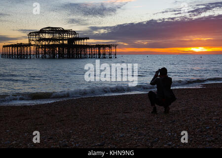 Brighton, UK. Eine junge Frau hockt ein Foto von einer spektakulären murmuration von Staren über verlassene von Brighton West Pier zu nehmen. Stockfoto