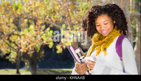 Ziemlich afrikanische amerikanische schwarze Studentin von SMS-Nachrichten oder über Handy. Zimmer für Kopieren oder Text über fallen Bäume im Hintergrund. Stockfoto