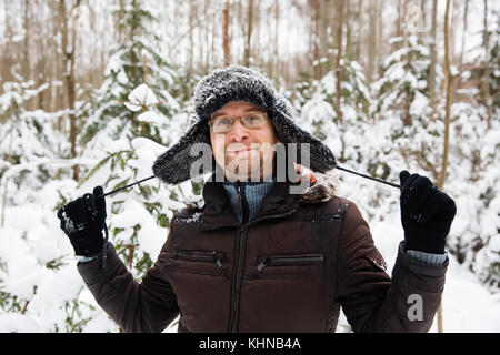 Mann in Fell winter Mütze mit Ohrenklappen lächelnd Portrait. extreme im Wald Stockfoto