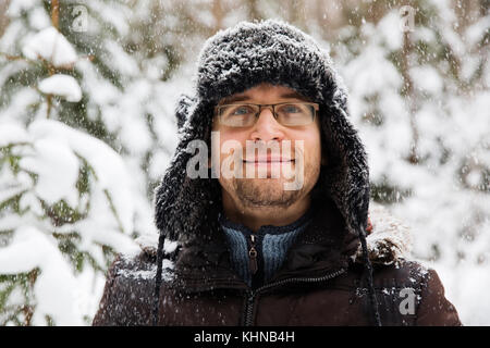 Mann in Fell winter Mütze mit Ohrenklappen lächelnd Portrait. extreme im Wald Stockfoto