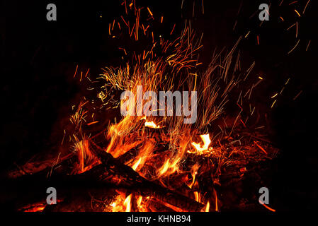 Rot und Orange Flammen der Scheiterhaufen und Funken in Form von Tracks auf schwarzem Hintergrund Stockfoto