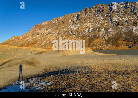 Die malerische Berg Herbst Landschaft mit Schnee bedeckte Berge, See, Sand Dünen mit spärlicher Vegetation gegen den blauen Himmel an einem sonnigen Stockfoto