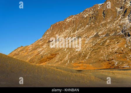 Die malerische Berg Herbst Landschaft mit Schnee bedeckte Berge, See, Sand Dünen mit spärlicher Vegetation gegen den blauen Himmel an einem sonnigen Stockfoto